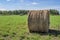 A roll of hay lies on a field of mown grass against a blue sky with clouds.