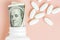 Roll of money Bills with Benjamin Franklin in white pill bottle with white oval pills around on pink background. medicine flat lay