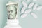 Roll of money Bills in white pill bottle with white oval pills around on Aqua Menthe background. medicine flat lay
