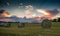 Rolled bales of hay are seen on a rolling hill during a magnificent sunset