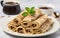 Rolled crepes or tiny pancakes with rich chocolate, displayed on a crisp white plate