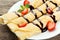 Rolled pancakes with strawberry on plate on grey wooden background.