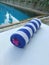 Rolled towel with pink flower on wooden sunbed and swimming pool