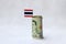 Rolled twenty baht banknote of Thailand and mini Thai flag on the white floor.