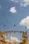 Roller coaster with waving flag photographed upwards against the bright and blue sky with sun and small white clouds