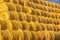 Rollers made of dry pressed yellow straw, stacked in a pyramid in a field, against a blue sky