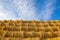 Rollers made of dry pressed yellow straw, stacked in a pyramid in a field, against a blue sky