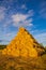 Rollers made of dry pressed yellow straw, stacked in a pyramid in a field, against a blue sky