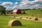 rolling farmland with red barn, horses, and hay bales