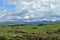 Rolling green fields with mountains and a cloudy sky. Criccieth, Wales.