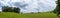 Rolling green meadows and emerald green hillside panorama with trees and stormy clouds, creative copy space