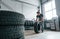 Rolls the tire. Adult man in grey colored uniform works in the automobile salon