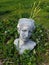 Roman head planter with cacti growning out of its head in a bed of ivy and grasses in the