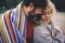 Romantic adult couple stay together with feeling and love covered by a woolen colorful blanket at the outdoor park. Concept of