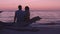 Romantic beach sunset couple honeymoon - Lovers enjoying watching sunset on summer travel destination sitting on tree
