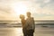Romantic biracial couple embracing while standing at beach against sky during sunset