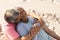 Romantic biracial senior man embracing happy senior woman from behind while sitting at beach