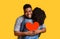 Romantic black man embracing girlfriend and holding red paper heart, making surprise