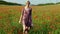 Romantic blonde woman with flower in hand walking in amazing poppy field.