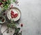 Romantic breakfast with porridge and heart of raspberries on grey kitchen table with flowers and bowls. Vegan breakfast idea with