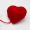 Romantic Christmas or Valentines Day concept. Red yarn ball like a heart on the white crochet background. Red heart made of wool y