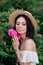 Romantic close-up portrait o charming brunette girl in straw hat smells flowers in rose bushes