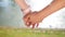 Romantic closeup of a young man`s hand holding a young woman`s hand when the happy couple is standing in the park near