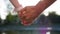 Romantic closeup of a young man`s hand holding a young woman`s hand when the happy couple is standing in the park near