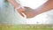 Romantic closeup of a young man`s hand holding a young woman`s hand when the happy couple is standing in the park near
