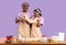 Romantic cooking times. Young black couple with dough baking on lilac background