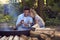 Romantic Couple Camping Sitting By Bonfire In Fire Bowl With Hot Drinks