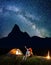 Romantic couple hikers looking at the shines starry sky at night. Happy pair sitting near camp and campfire