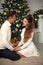 Romantic couple portrait in love. Cheerful Happy newlywed hugging by Xmas Christmas tree. Man propose marriage his girlfriend. Win