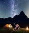 Romantic couple is sitting near the glowing tent and campfire and looking to the stars in the night sky