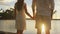 Romantic couple at sunset holding hands at beach watching the sun set honeymoon