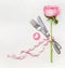 Romantic dinner table place setting with fork, knife , pink rose and heart on white wooden background, top view. Love symbol