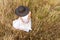 Romantic dreamy top view scene of unrecognizable woman sitting in a field of wheat and tall yellow grass wearing a dark wide-