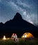 Romantic family tourists covered with a plaid sitting together near campfire and shines tent at night