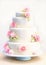 Romantic four tiered wedding cake, with pastel pink rose flowers, on a blue stand. Watercolour style with paint splatters and