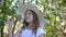 Romantic girl sniffing flowering apple tree in spring garden at sunny day. Smiling girl teenager in white hat enjoying