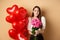 Romantic girlfriend smelling roses, receive flowers from lover on Valentines day, standing near red hearts balloons and