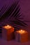 Romantic home decor in tropical style with burning candles and palm leaf in evening purple and orange light, vertical, closeup.