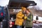 Romantic journey winter camper vacation, man kisses woman while drinking hot tea in cups standing at mini camper back