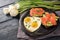 Romantic meal with love, fried eggs in heart shape, sandwiches with avocado and smoked salmon, white tulips on a dark blue rustic