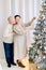 Romantic middle aged couple in love spending time together, while decorating Christmas tree. Hansome man kissing his