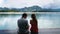 Romantic Pair of Man and Woman Sitting on Wooden Lake Pier with Green Mountains