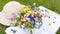 A romantic photo of a cute spring bouquet of forget-me-nots and daisies lying on a book of poems next to a sun hat on a green lawn