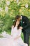 Romantic picknick in park. Drinking tea under tree, decorated with small glass lanterns. Groom is gently kissing his charming wife