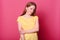 Romantic pretty young lady looking directly at camera, has shy facial expression, posing over pink background. Studio shot of girl