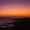 Romantic scenic sunset on the coast with black. rock beach and quiet wave ocean - sky and clouds in background - red and orange